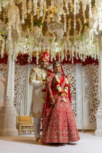 Beautiful Indian couple in traditional attire during wedding ceremony under floral canopy.