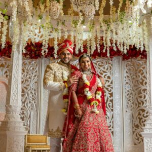 Beautiful Indian couple in traditional attire during wedding ceremony under floral canopy.