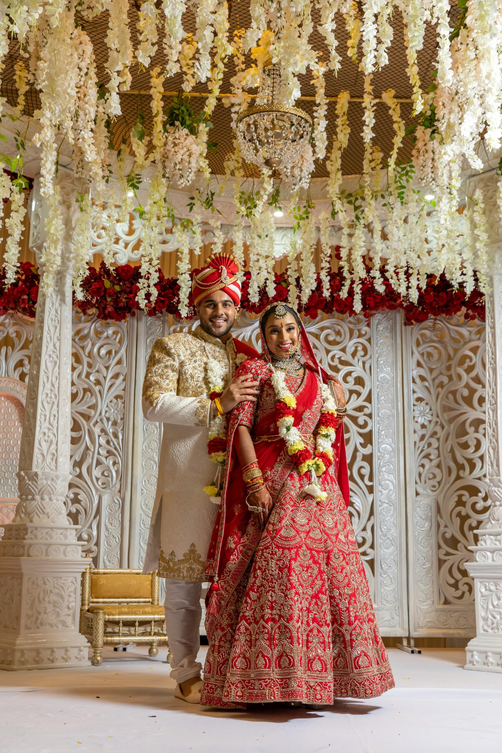 Beautiful Indian couple in traditional attire during wedding ceremony under floral canopy.